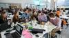 A group of young men and women sitting at tables in groups taking part in a hackathon